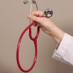 A close-up shot of a hand holding a red stethoscope against a plain background, emphasizing medical themes.