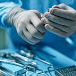 Close-up of surgeon's hands preparing tools for surgery in operating room.